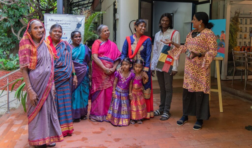 People and children stand in a group, some wearing beautiful saris and smiling.